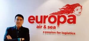 Hugo Feng, General Manager Shanghai Office, stands in front of a red Europa Air & Sea sign